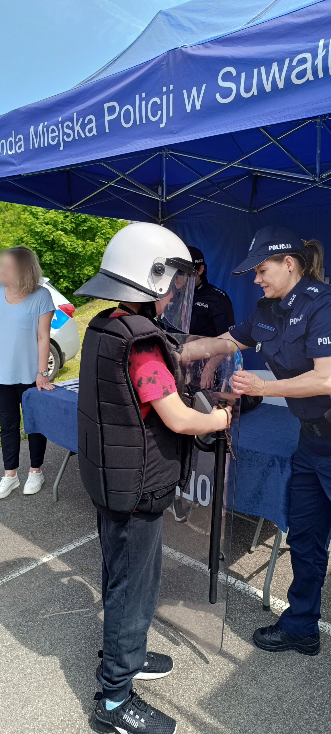 Policjantka pomaga dziecku założyc mundur szturmowy polskiej policji