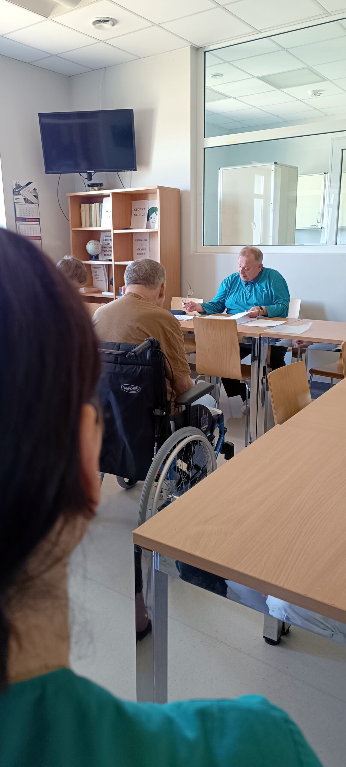 Starszy i grubszy mężczyzna prowadzi wykład na temat szkodliwości palenia papierosów. Trzyma okulary w lewej ręce