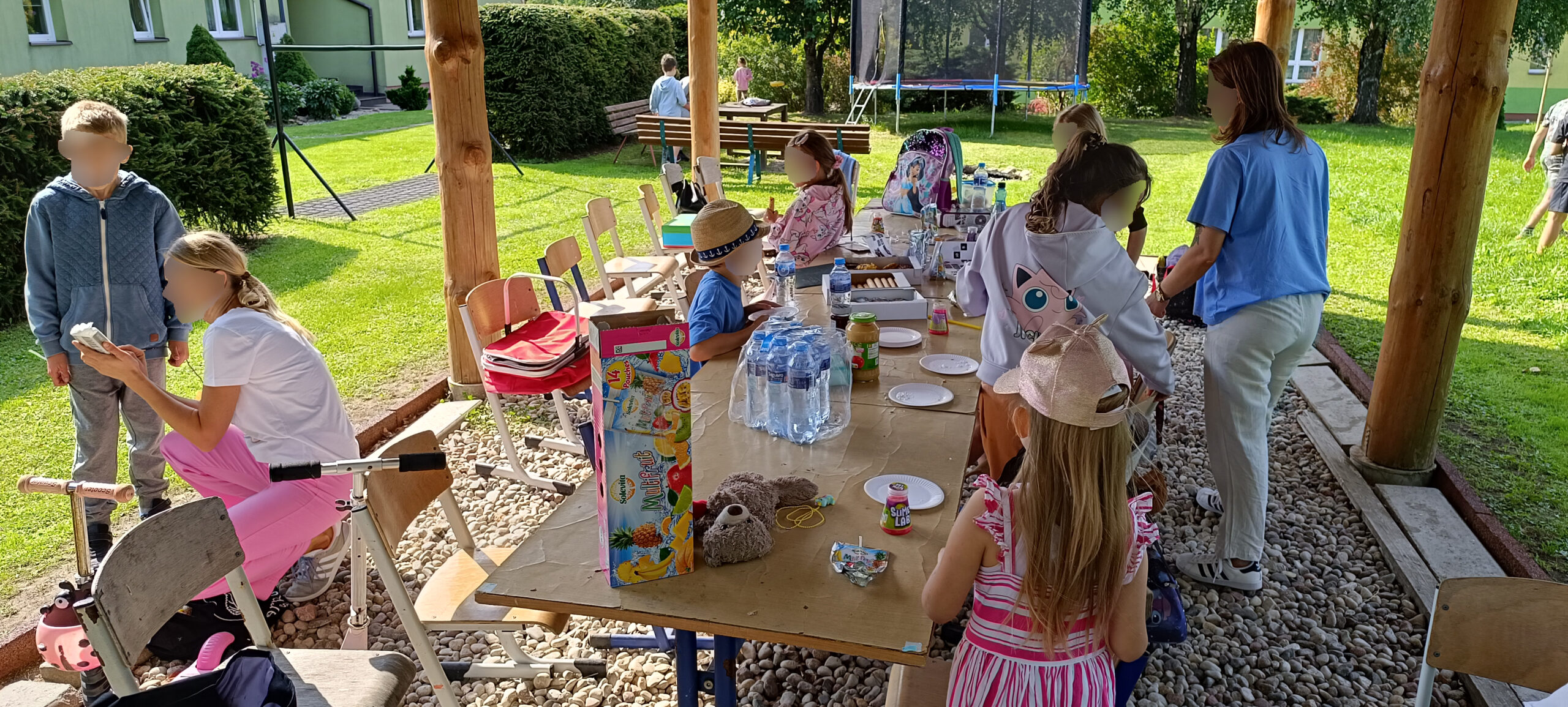 słoneczny dzien podwórko dzieci jedzą posiłek pod wiatą