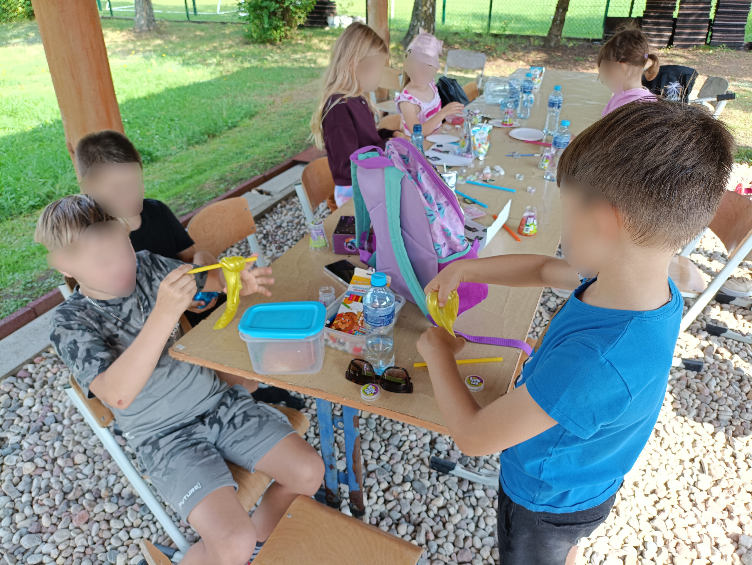 stół i wiata a pod wiata grupa dzieci spożywa posiłek . Wszystko na podwórku w pogodny dzień