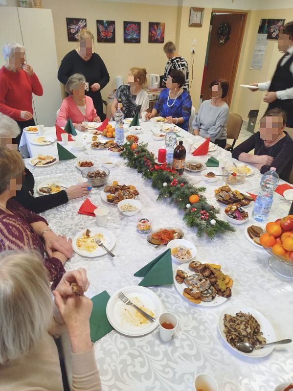 Grupa osób siedzi przy uroczyście zastawionym stole wigilijnym