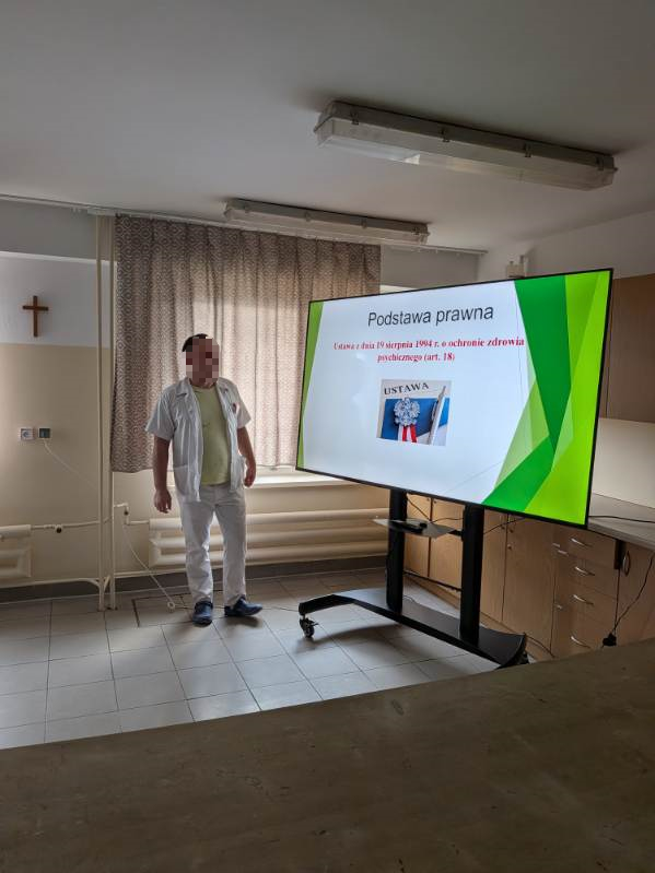 Mężczyzna stoi na sali przed 85 calowym telewizorem Opowiada na temat wyświetlanego obrazu