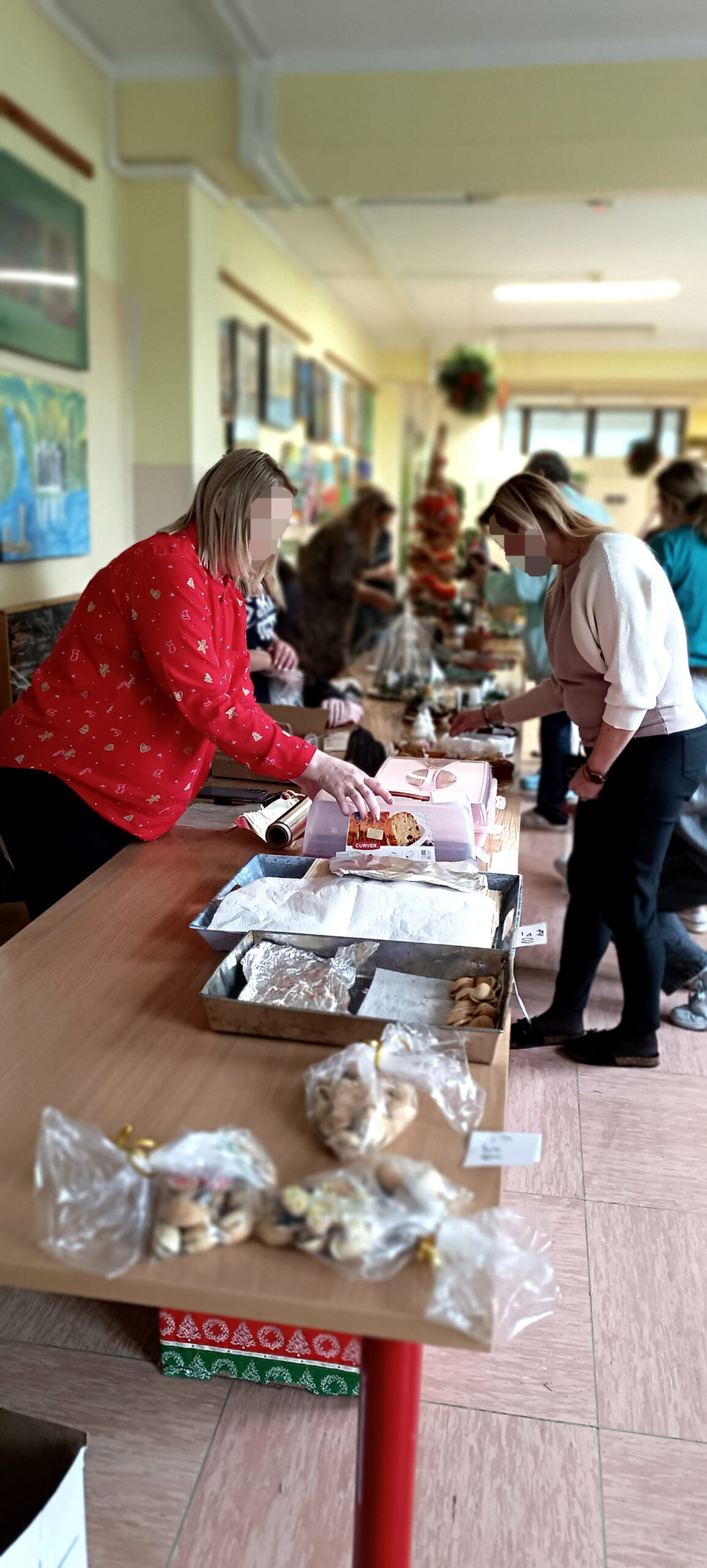 Grupa ludzi  ogląda stroiki i ozdoby świateczne wystawione na szkolnych ławkach w korytarzy szpitala