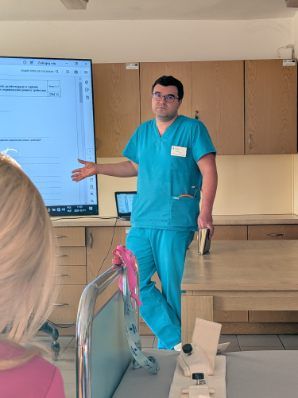 Mężczyzna stoi na sali przed 85 calowym telewizorem Opowiada na temat wyświetlanego obrazu