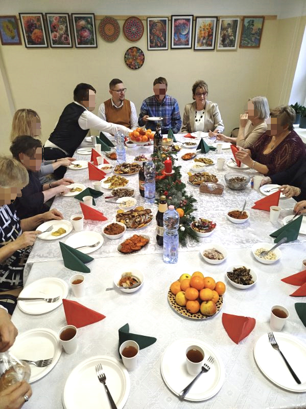 Grupa osób siedzi przy uroczyście zastawionym stole wigilijnym