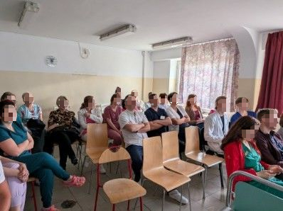 Grupa kobiet i mężczyzn słucha na siedzaco wykładu w małej salce.