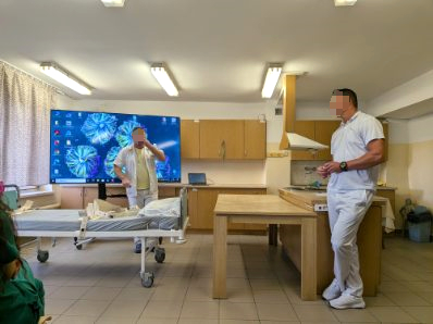 Dwóch mężczyzn stoi na sali przed 85 calowym telewizorem Opowiada na temat wyświetlanego obrazu