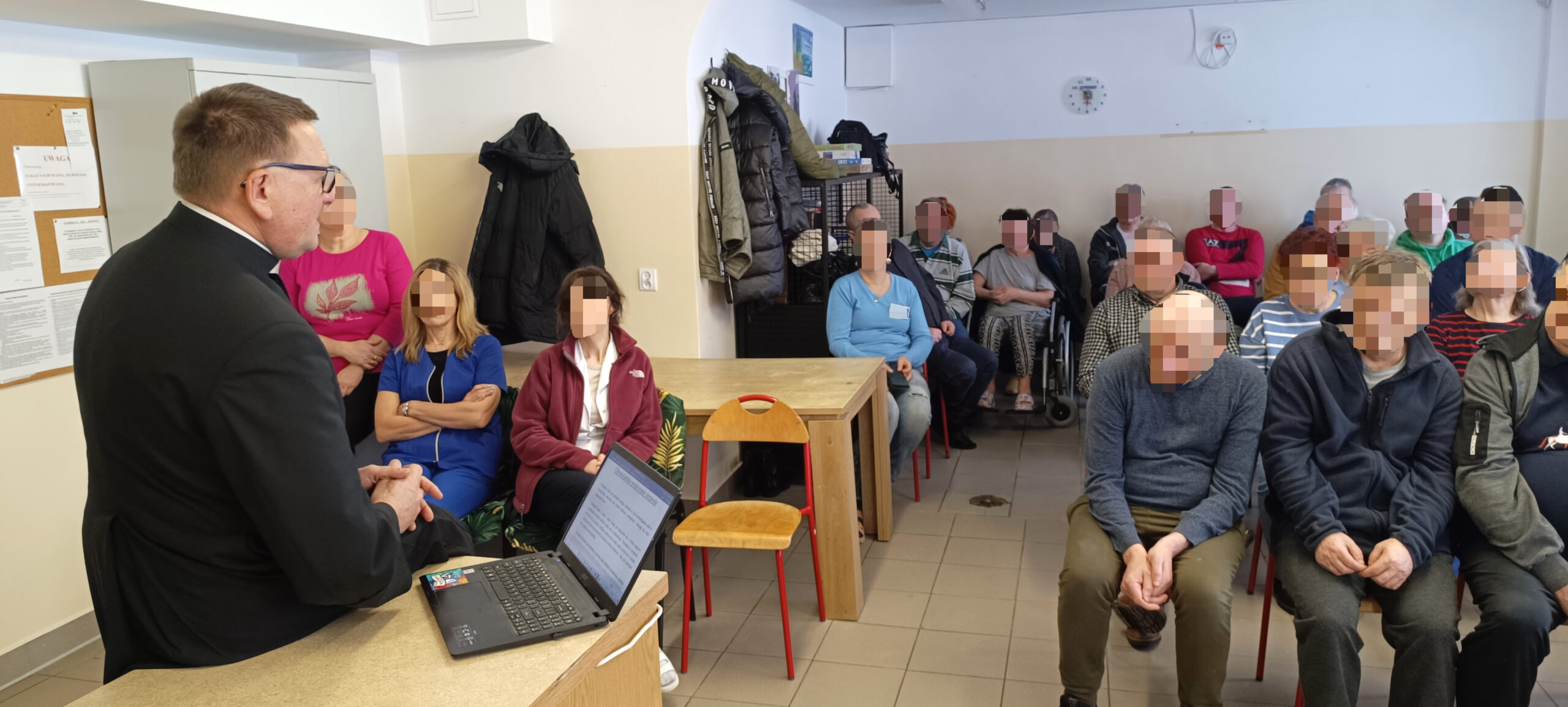 Mężczyzna w sutannie w sali kulinarno konferencyjnej prowadzi wykład dla duzej grupy ludzi