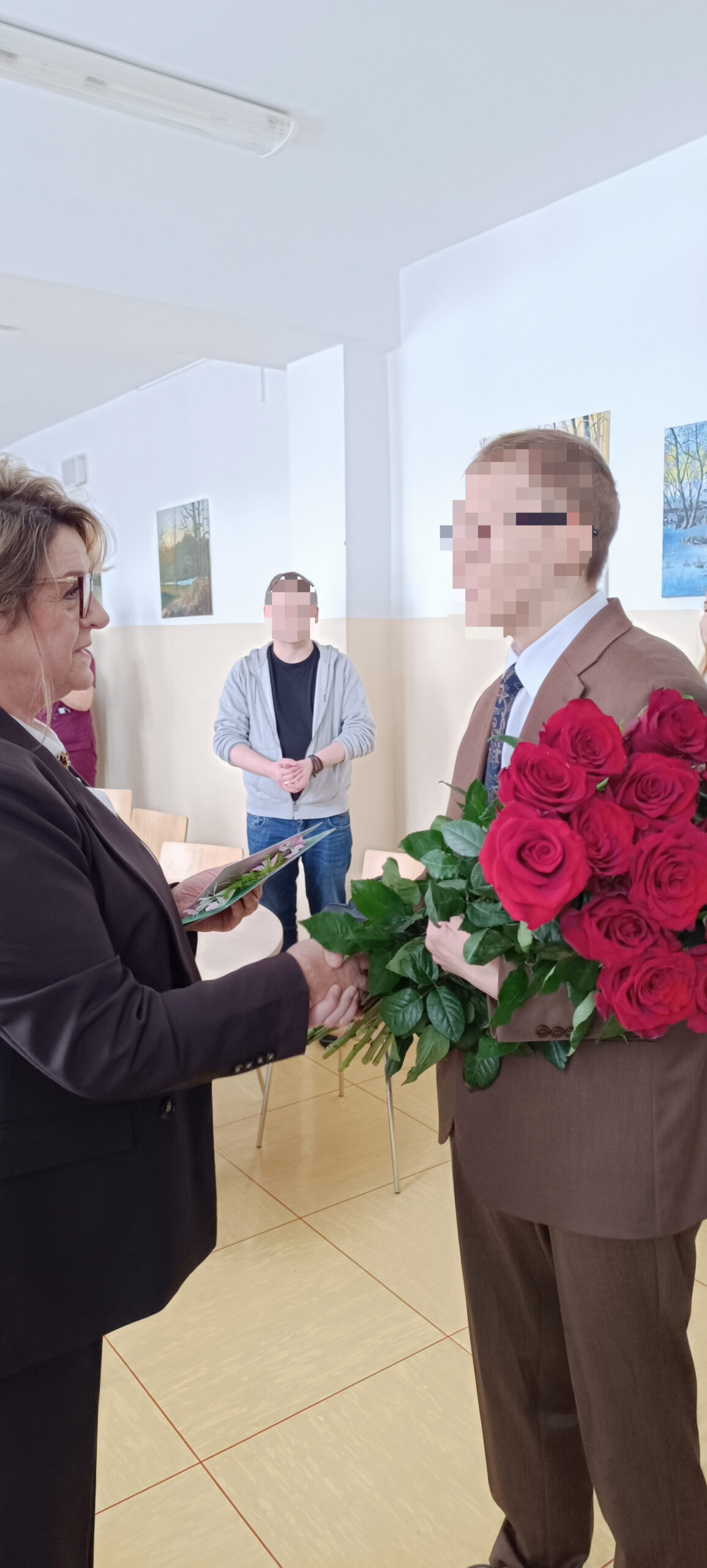 Młody chłopak wręcza kwiaty (róże) kobiecie na sali konferencyjnej