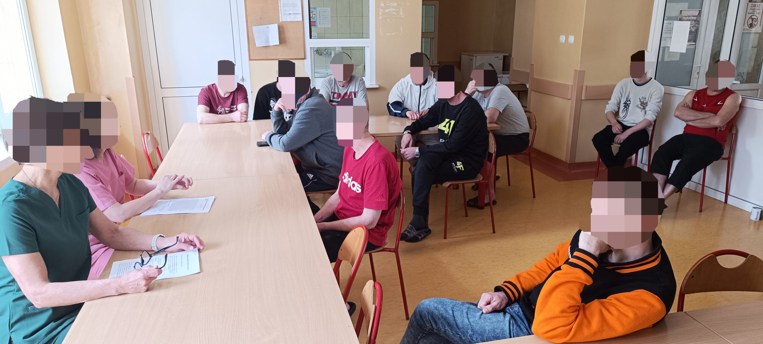 Stołówka w szpitali, gruba mężczyzn siedzi i słucha wykładu.