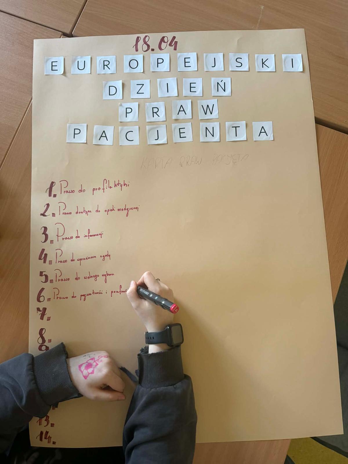 Kawałek kartki papieru na krórej widać rękę która rysuje i wkleja elementy i treści stanowiące częśc plakatu. 