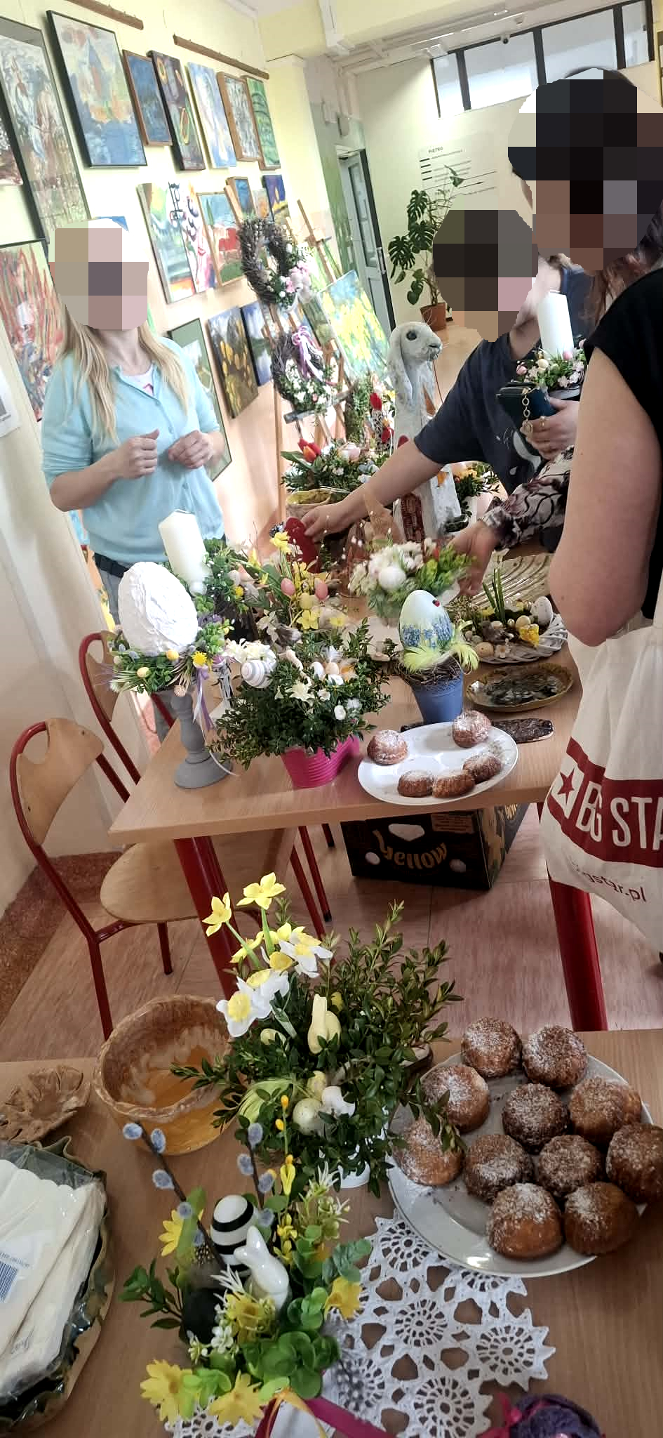 sala szpitalna wystawa prac wielkanocnych , dużo ludzi, na stołach rozstawione świątecznestroiki, , młodzież robi gofry