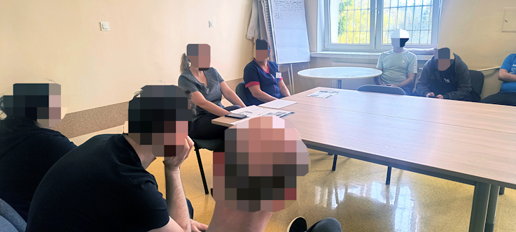 Sala konferencyjna, gruba mężczyzn siedzi i słucha wykładu.