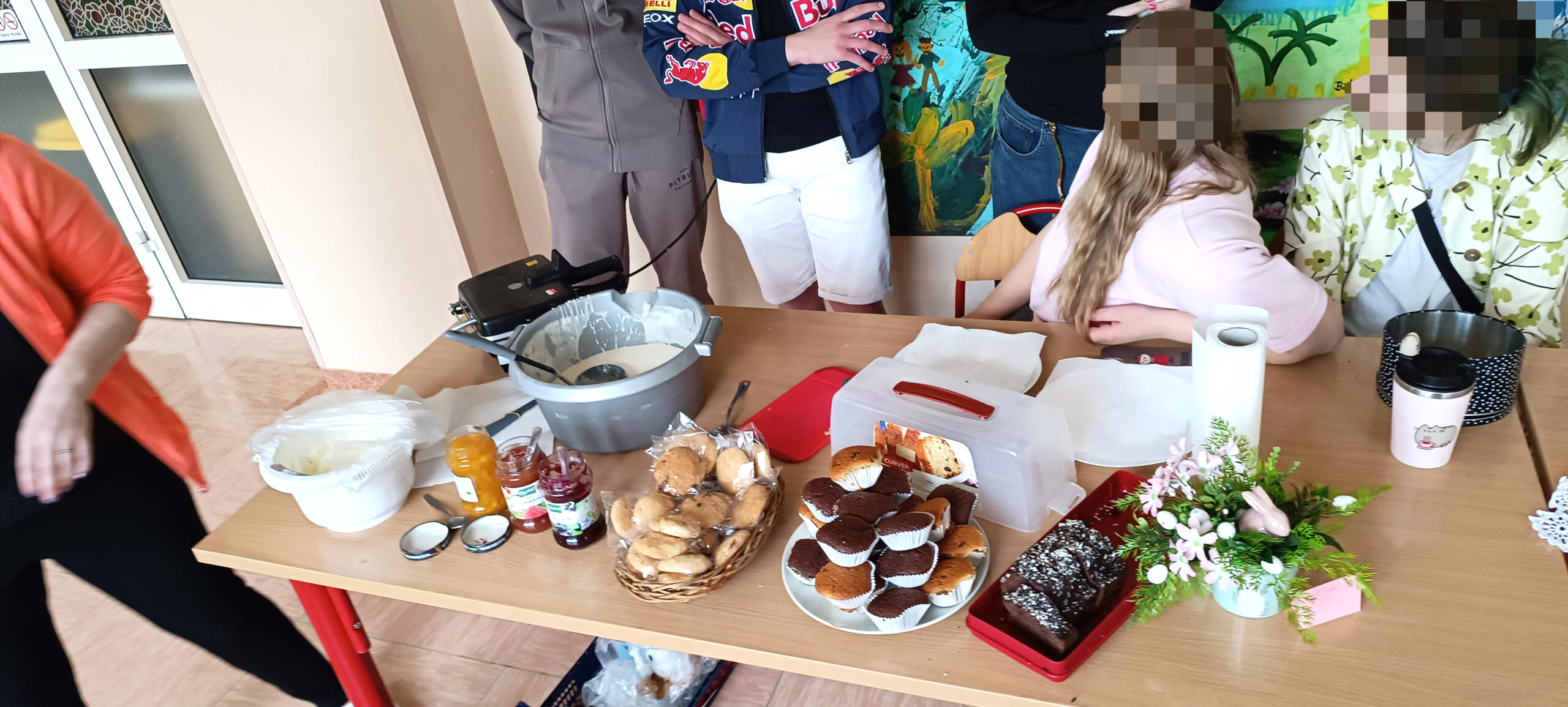 sala szpitalna wystawa prac wielkanocnych , dużo ludzi, na stołach rozstawione świątecznestroiki, , młodzież robi gofry