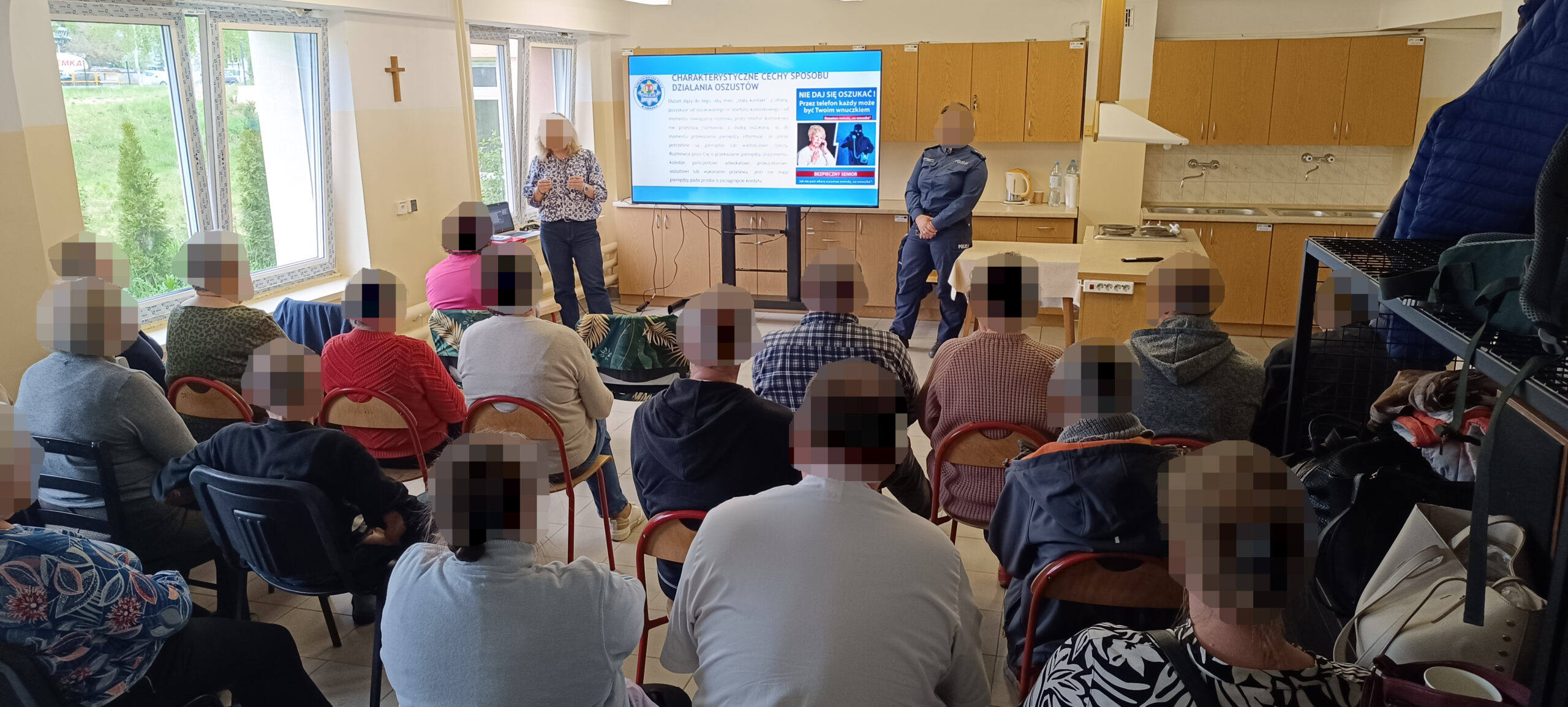 Wykład na salce w ciągu dnia, w tle telewizor z informacjami które pokazuje kobieta razem z policjantką w mundurze