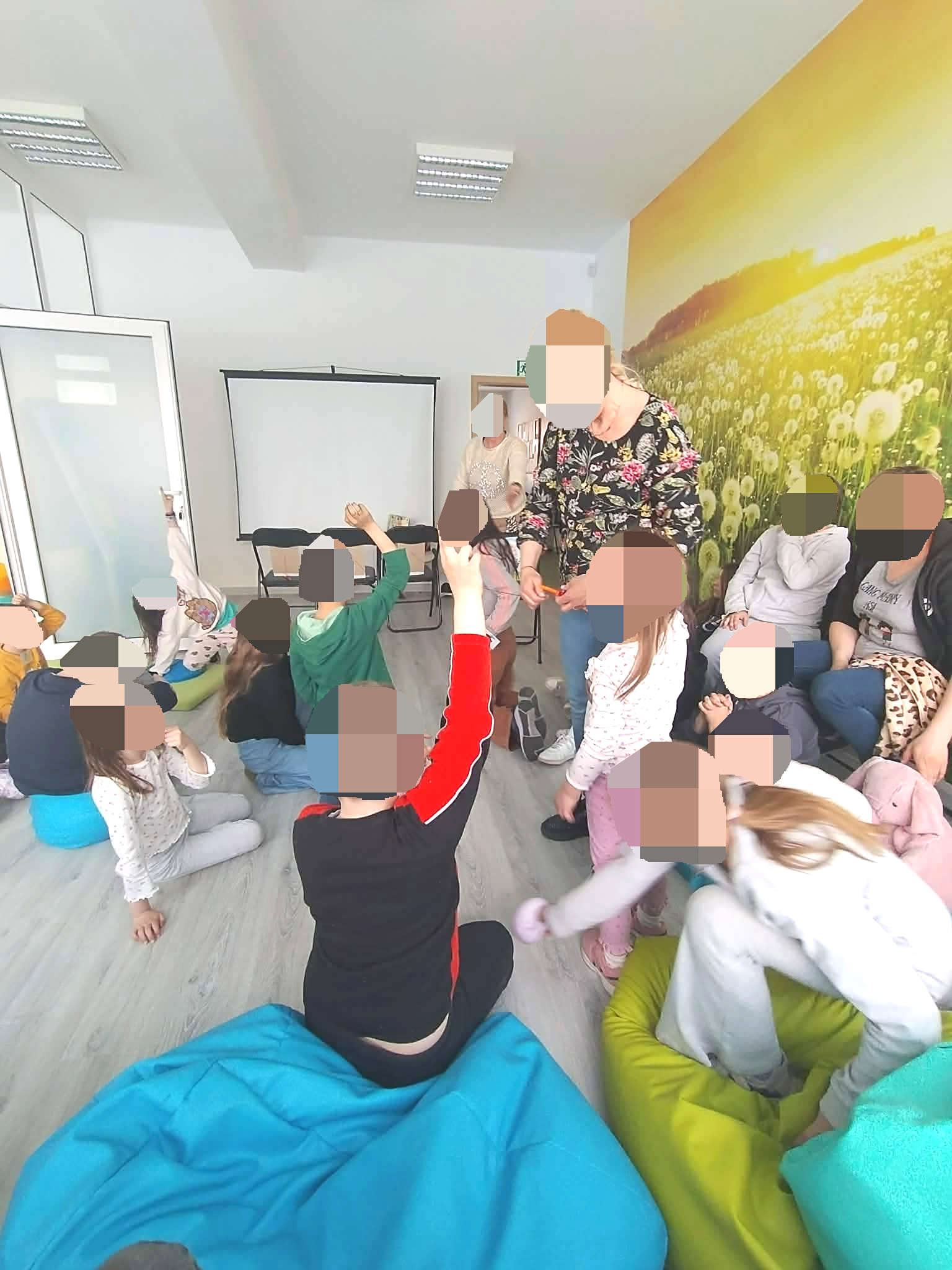 Wiosenne warsztaty w augustowie, Grupa dzieci uczestniczy w zajęciach z opiekunami w pomieszczeniu w ciągu dnia. Widać aktywną zabawę, podnoszenie rąk do góry w celu chęci odpowiedzi na zadane pytania 